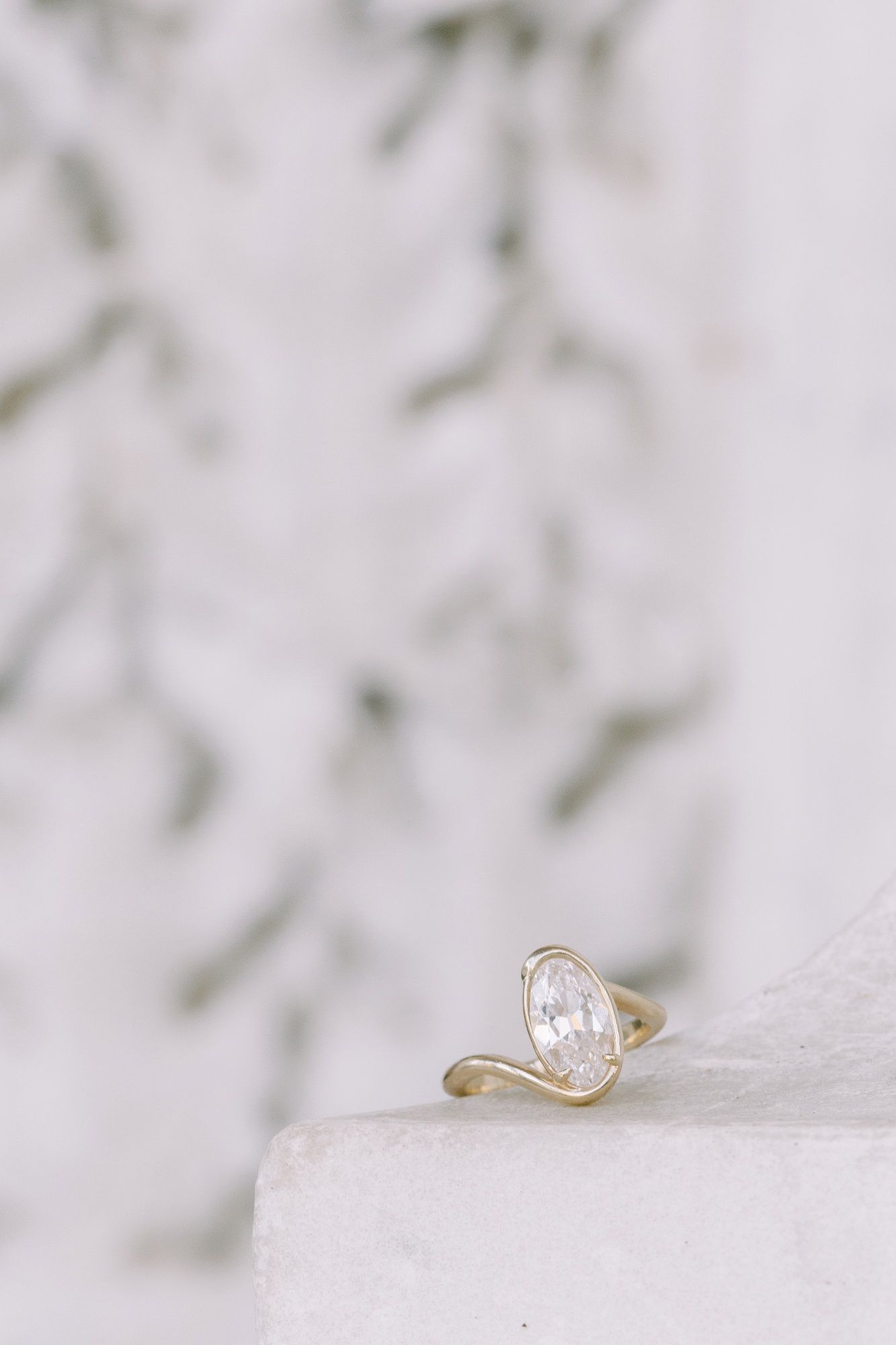 A delicate gold ring with a small pearl and diamond accent sits on a white textured surface.