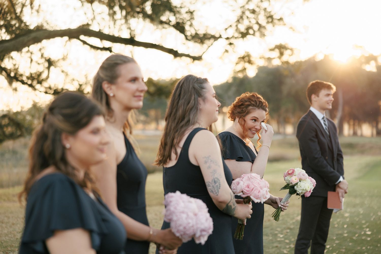 Wedding party laughs together while walking outdoors at golden hour.