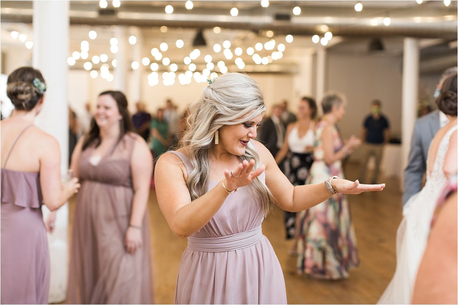A bridesmaid in a dusty rose dress dances joyfully at a wedding reception.