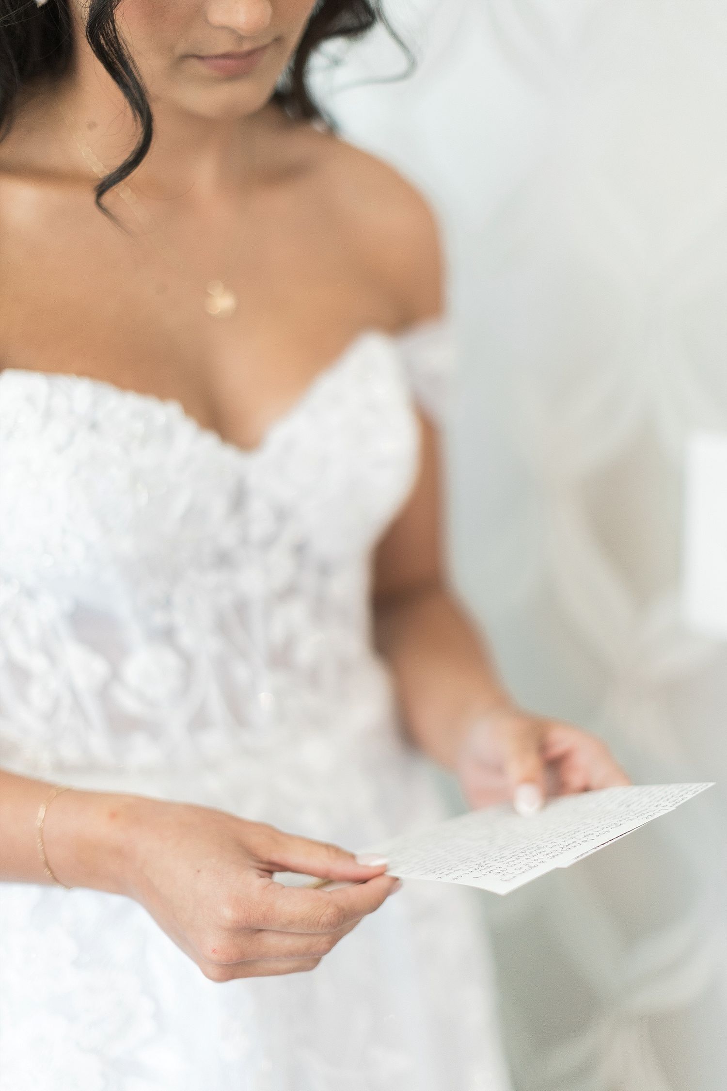 Close-up of a bride in lace dress holding a piece of paper.