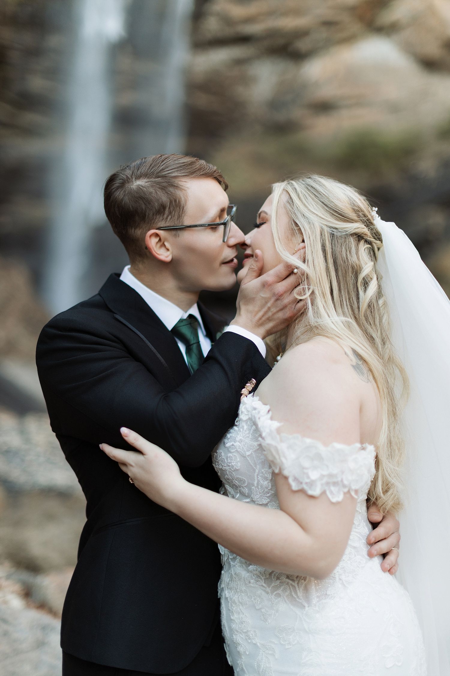 A romantic wedding moment captured in front of a waterfall as a couple shares an intimate embrace.