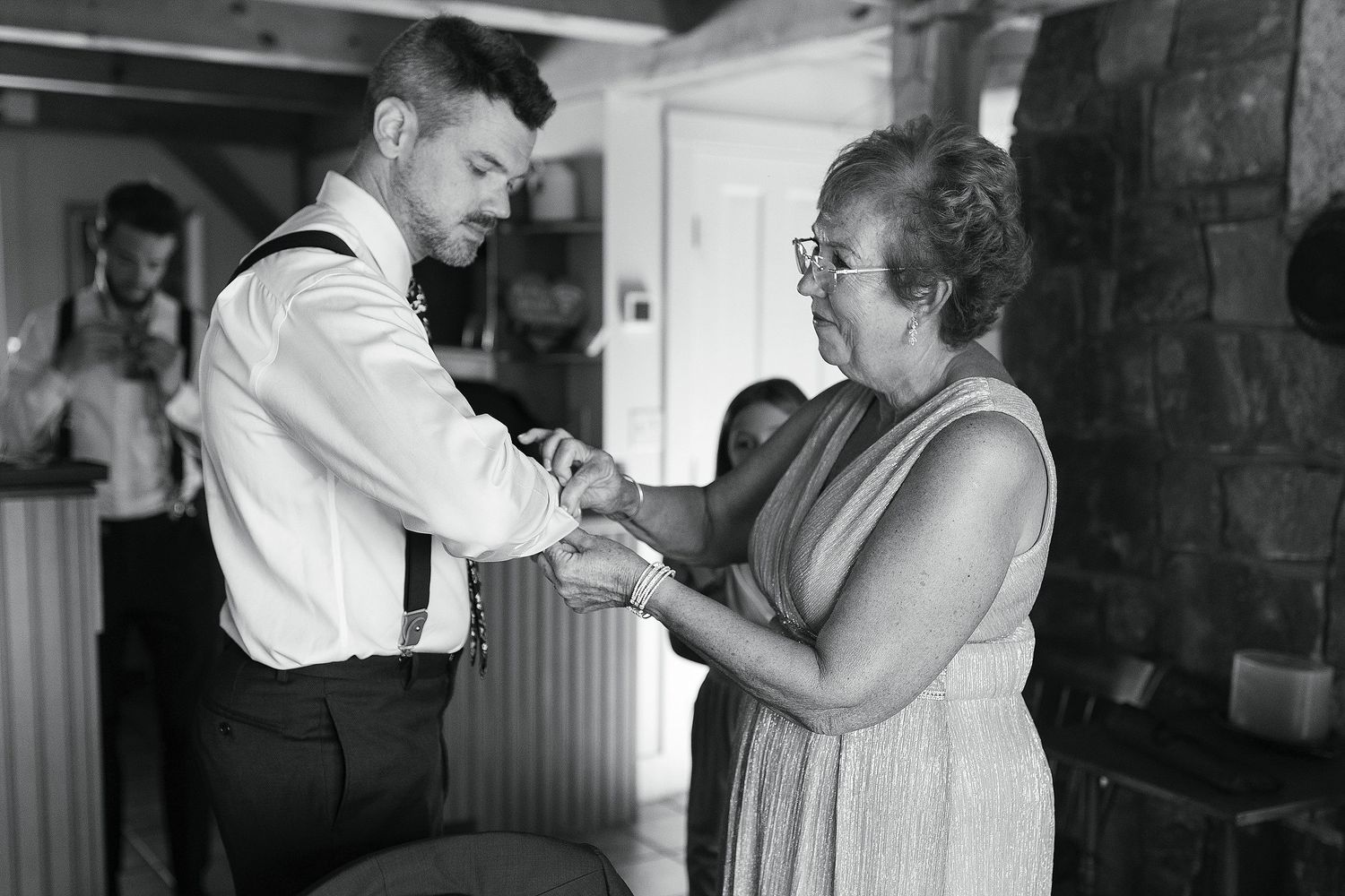 A tender moment captured in black and white as a young man and elderly woman hold hands during a wedding preparation.