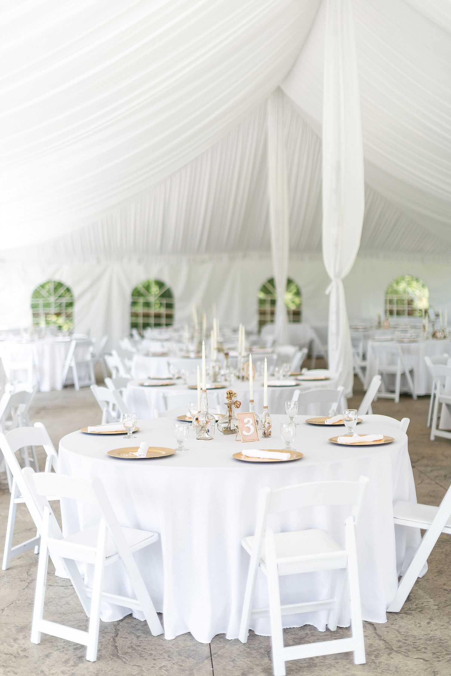 White wedding reception tent interior with round tables, white linens, and elegant place settings.