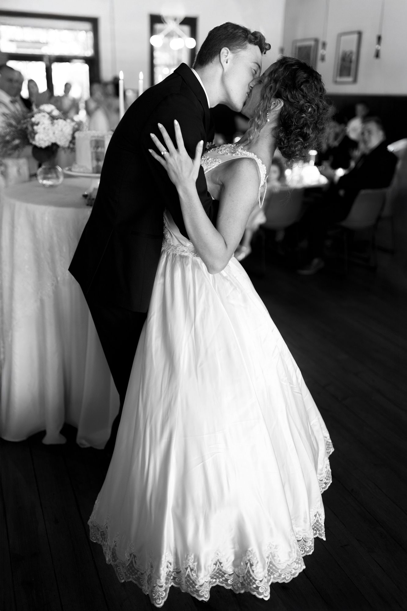 Black and white photo of bride and groom sharing first dance kiss at wedding reception.