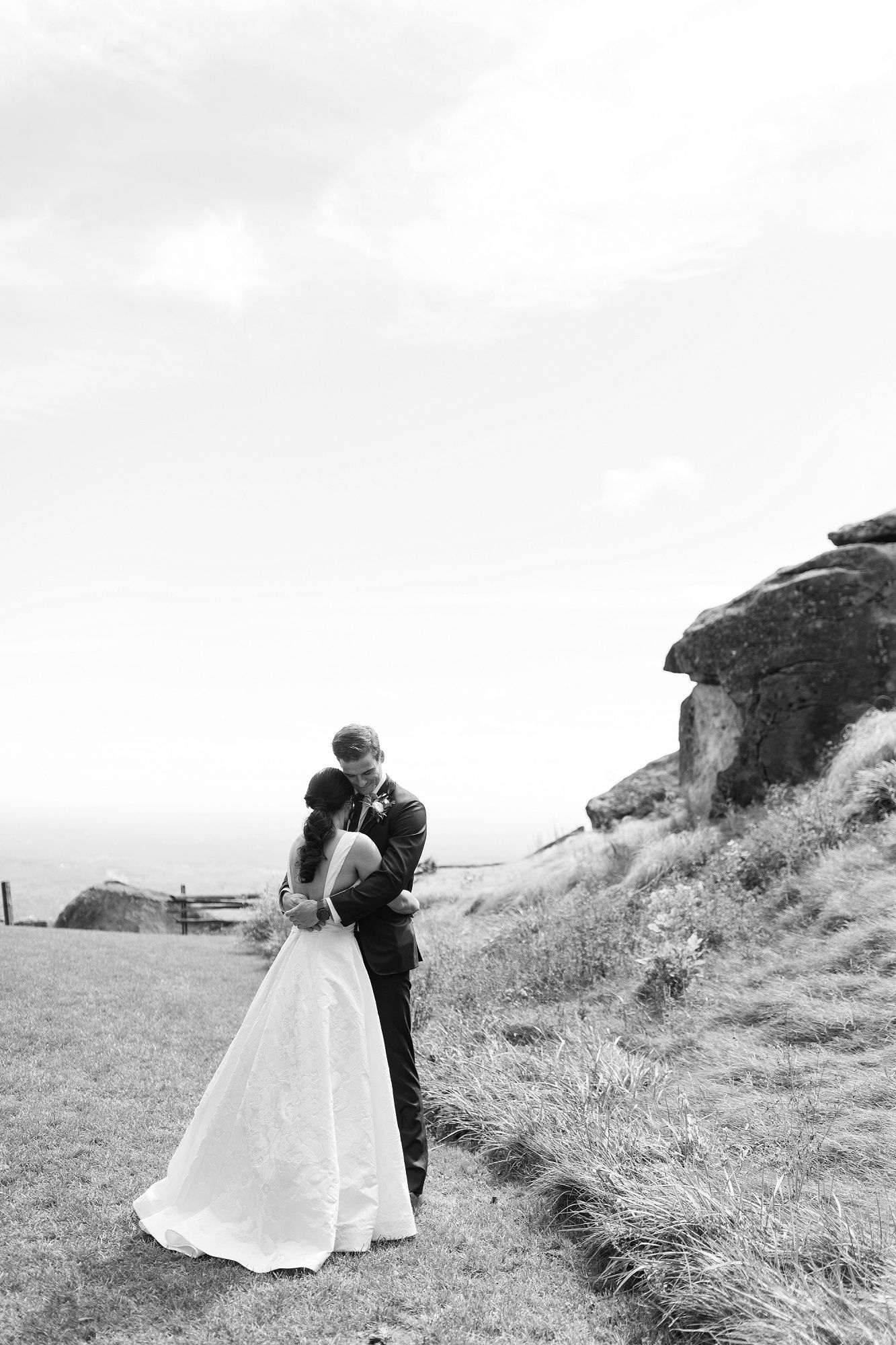 Black and white wedding portraits captured on a windswept coastal hillside.