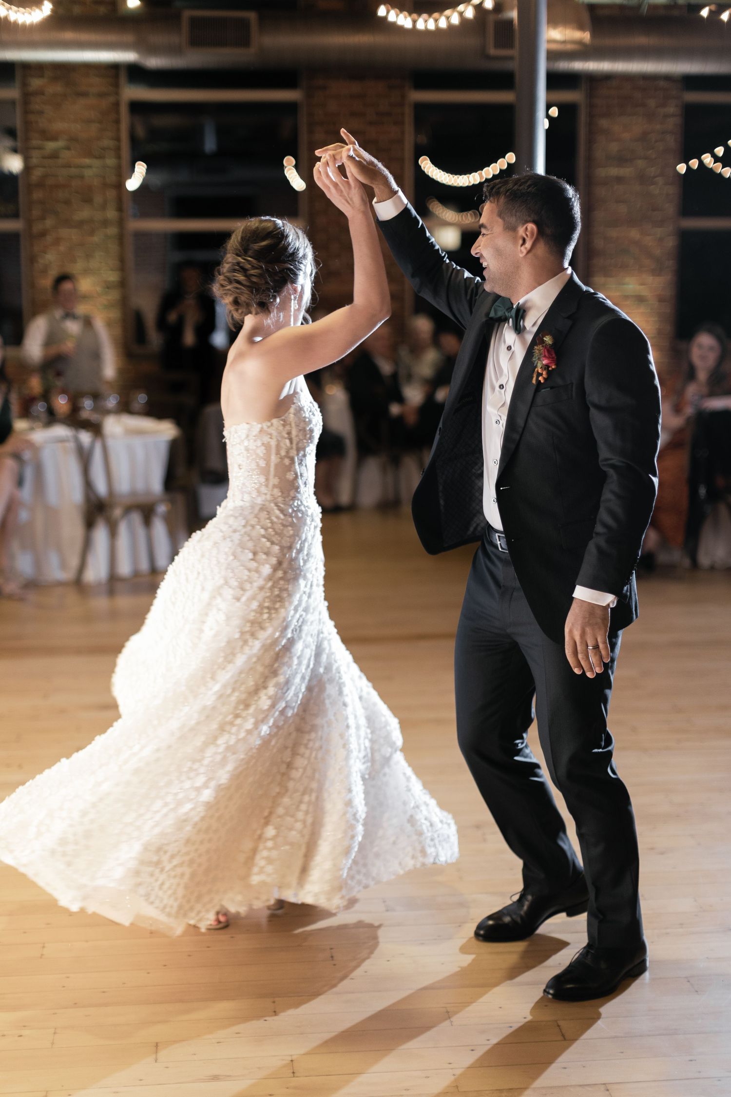 Bride and groom dancing together at wedding reception, groom spinning bride on dance floor.