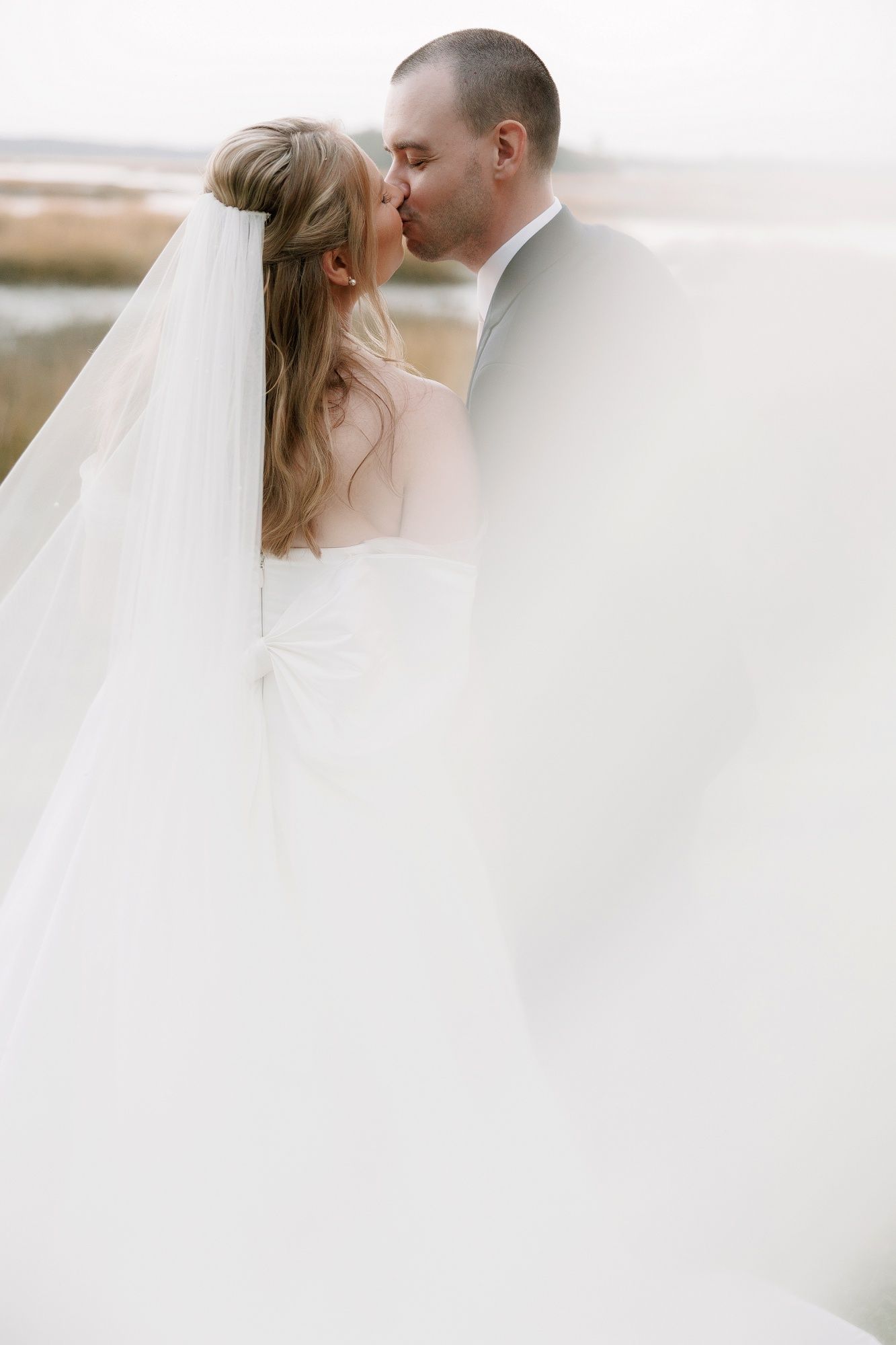 A romantic wedding portrait with flowing white veil against a bright background.