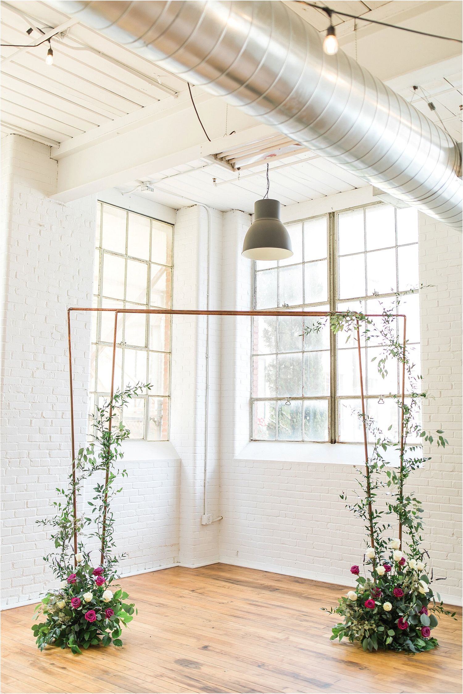 Modern industrial wedding venue with exposed ductwork, white brick walls and floral arrangements.