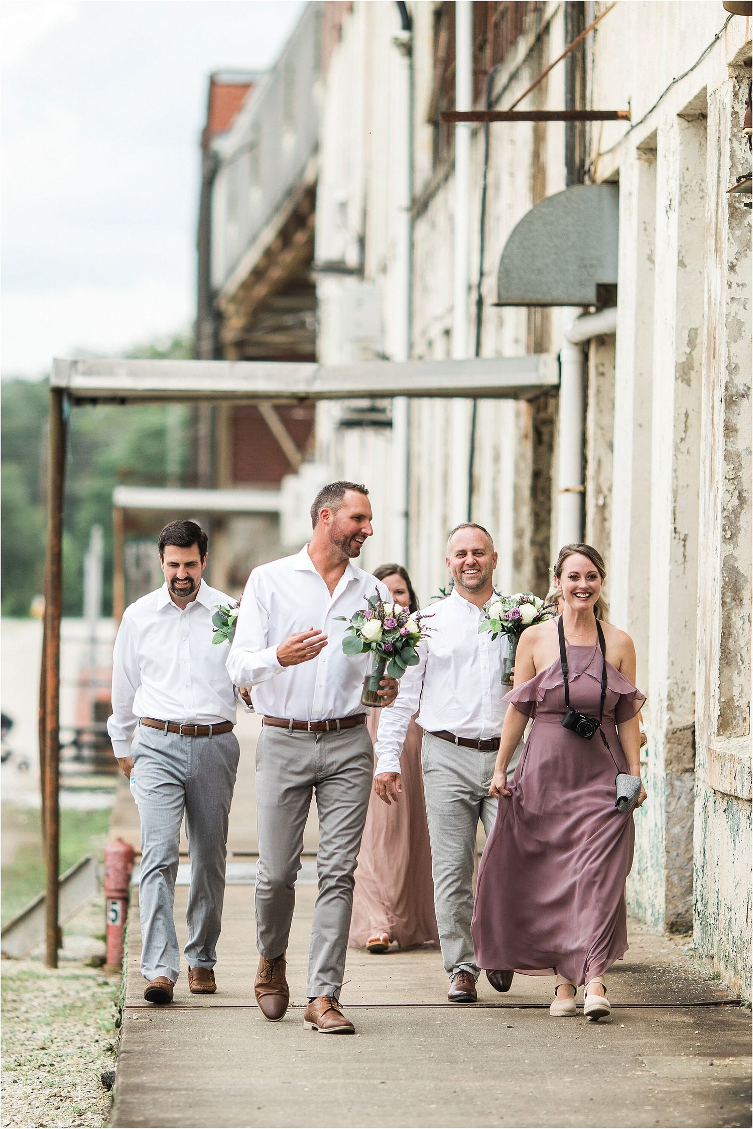 Wedding party walks along historic building sidewalk in casual attire.