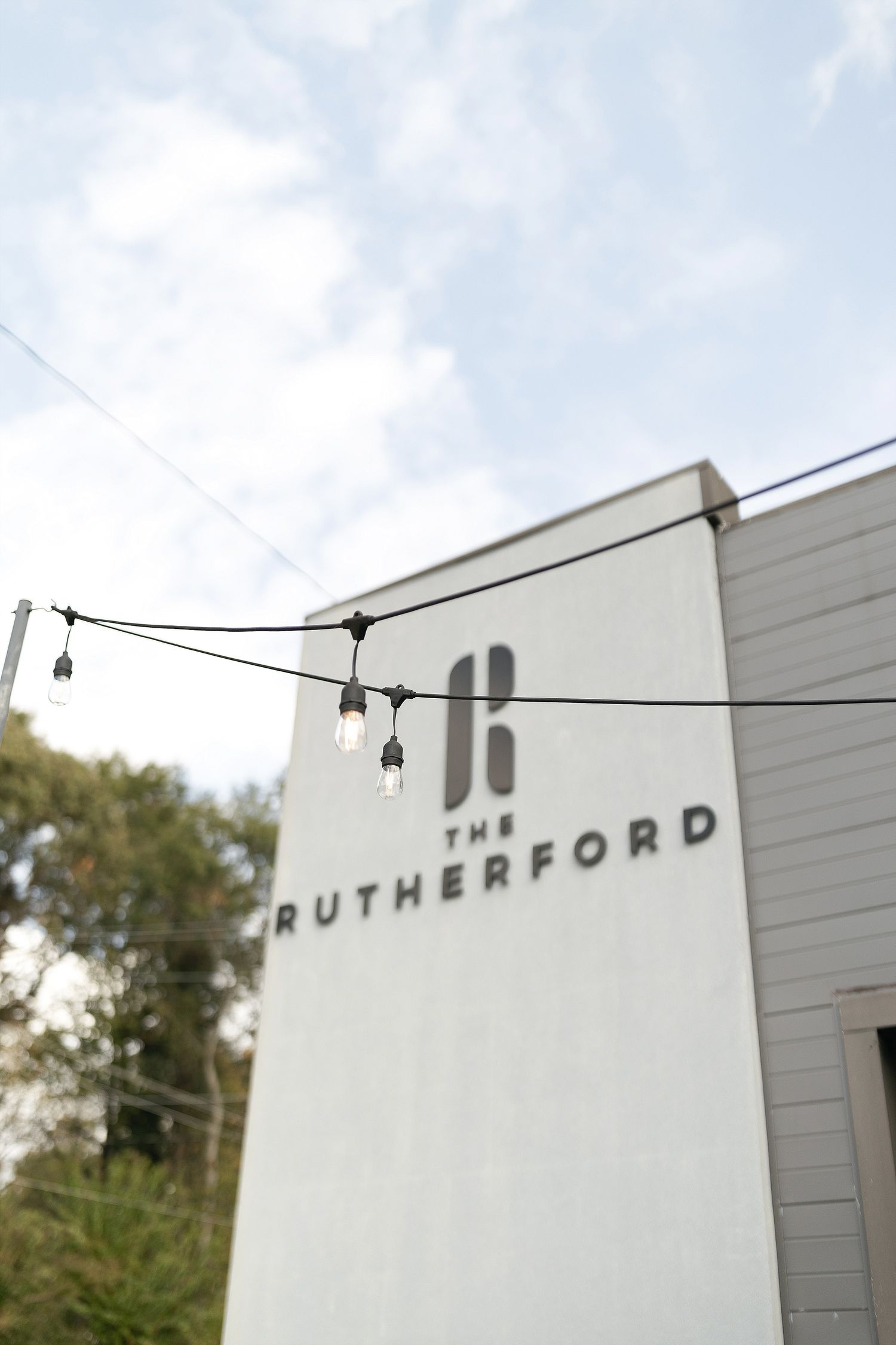 White building exterior with Rutherford signage and string lights hanging above against a cloudy sky.