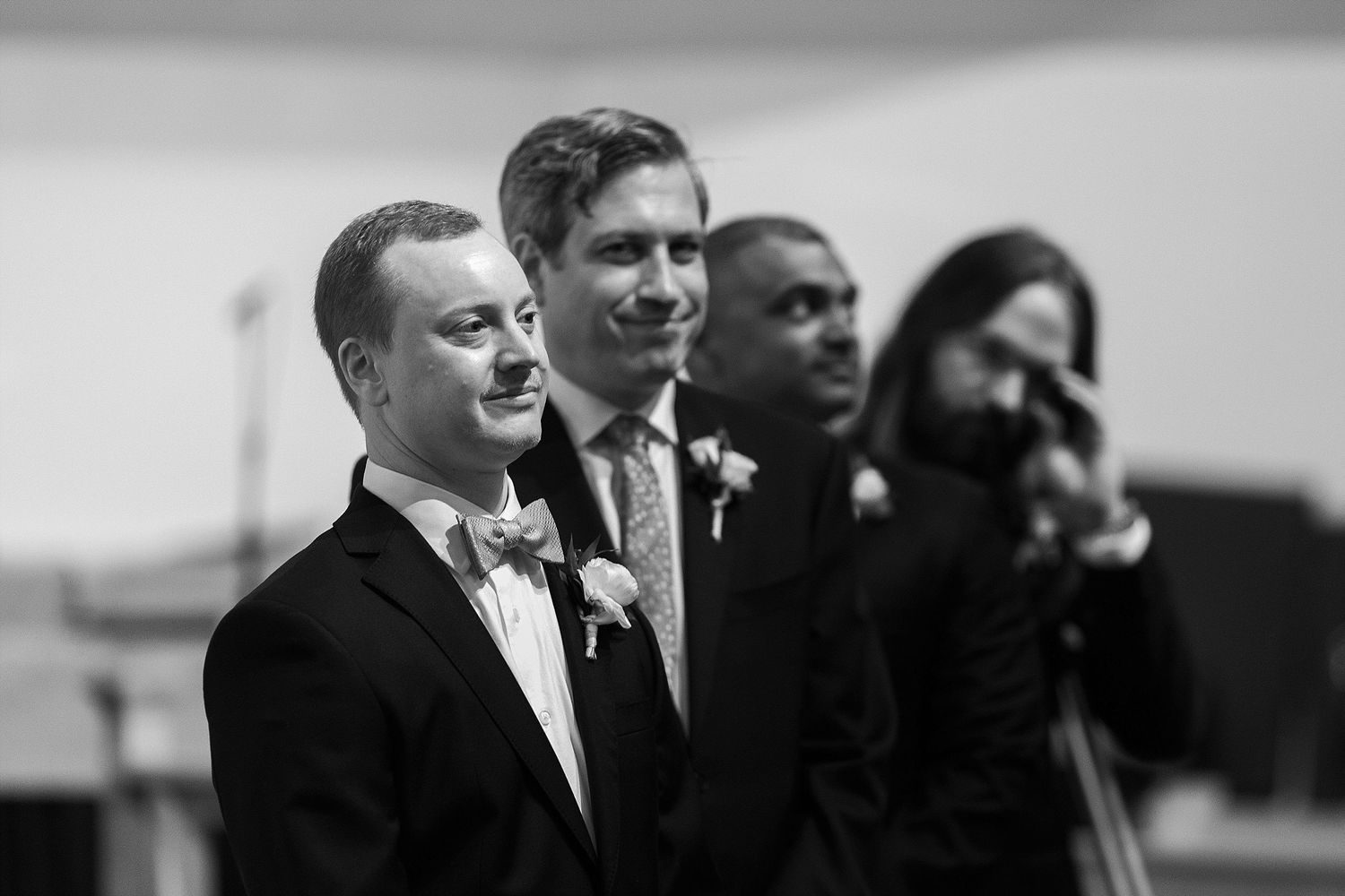 Groomsmen share an emotional moment during wedding ceremony in black and white photography.