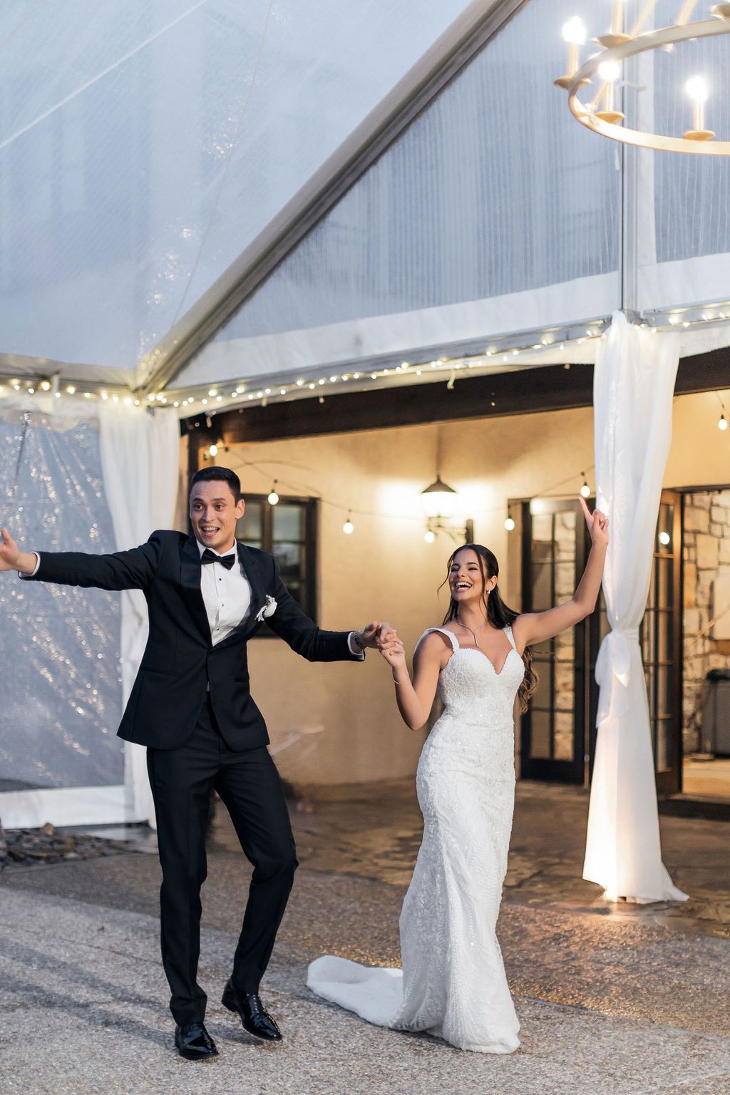 A couple celebrates during their wedding reception entrance in a beautifully lit tent venue.