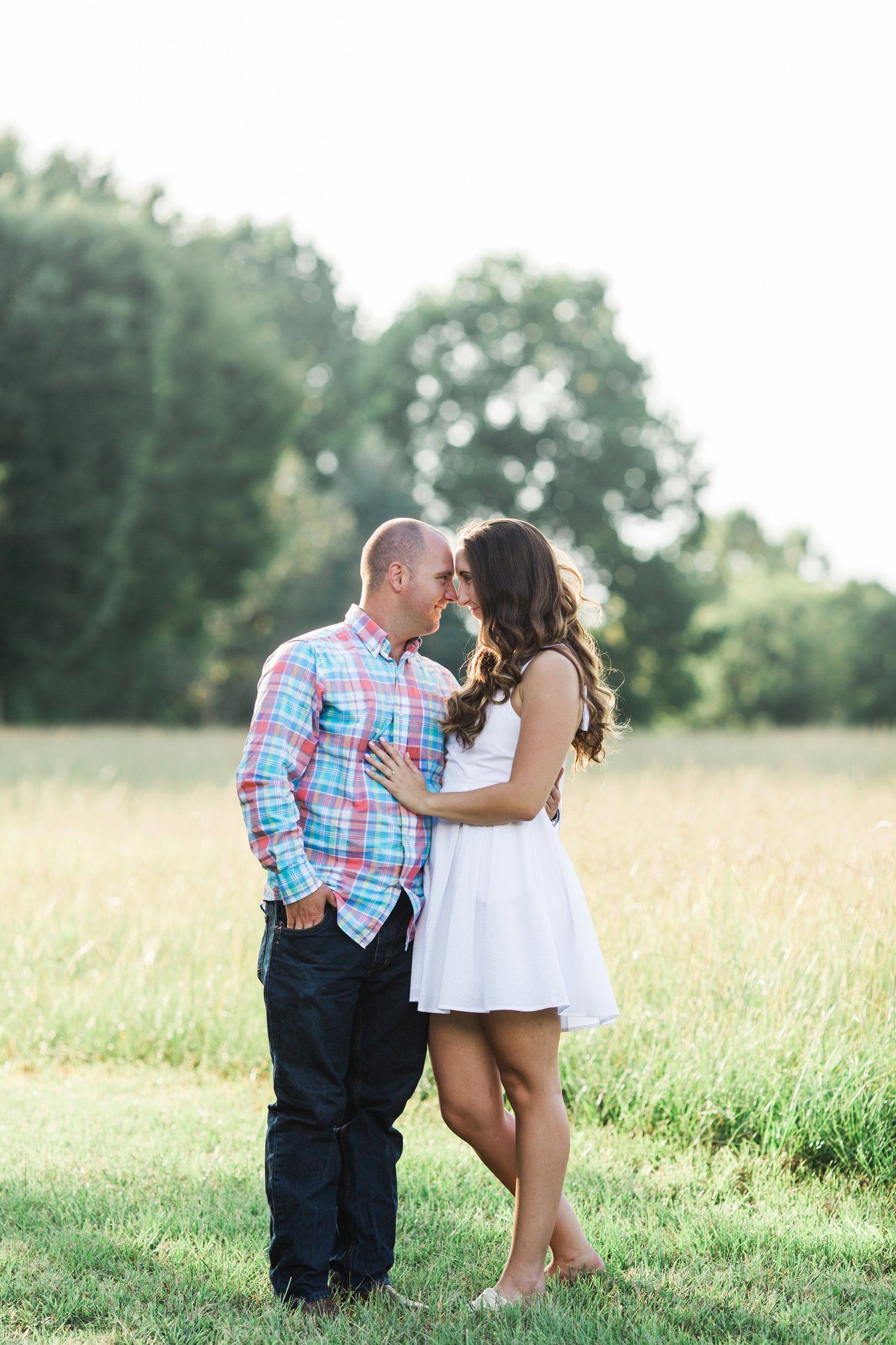Romantic couple poses together in sunny meadow during summer engagement photoshoot.