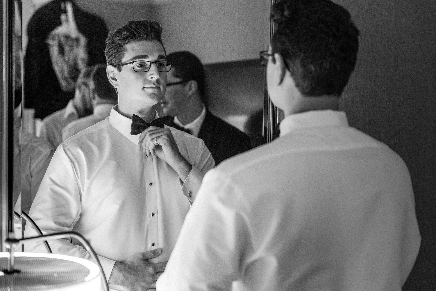 A formal preparation scene with bow ties and tuxedos being adjusted in a mirror.