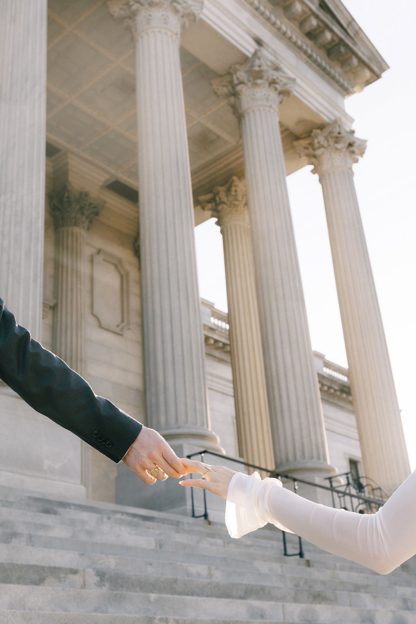 A series of cropped photos showing hands reaching out between classical stone columns of a grand building.