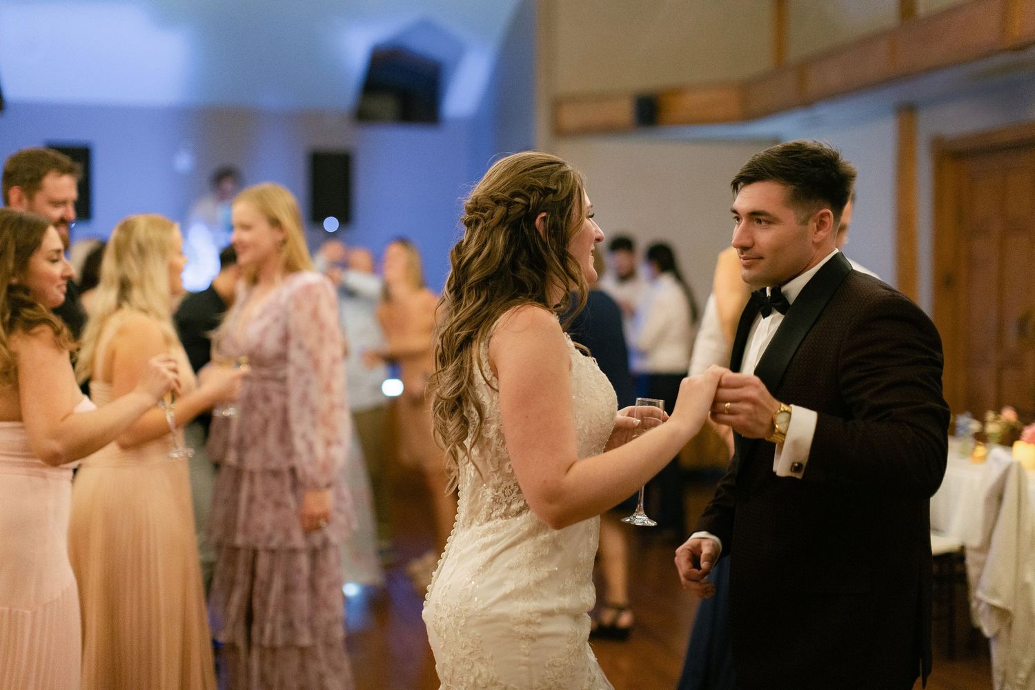 A group dances together in a blue-lit reception hall during a formal celebration.
