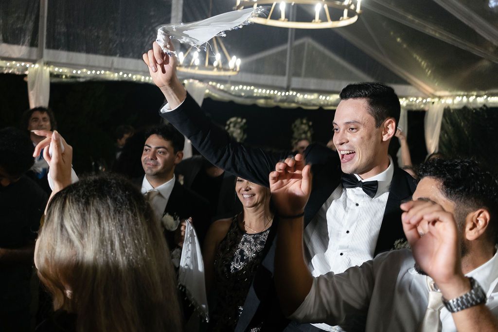 Energetic party scene with guests celebrating and dancing under string lights at an evening reception.