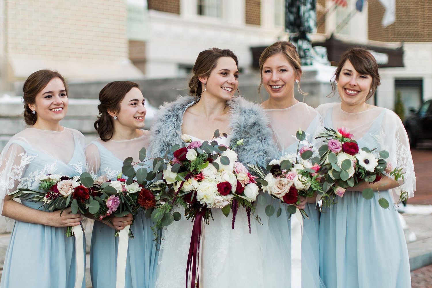 Wedding party of bridesmaids in pale blue dresses holding elegant floral bouquets.