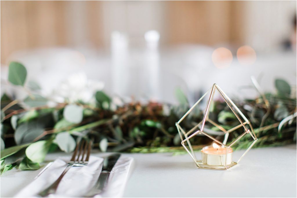 Modern geometric gold centerpiece with eucalyptus leaves on a white tablescape.