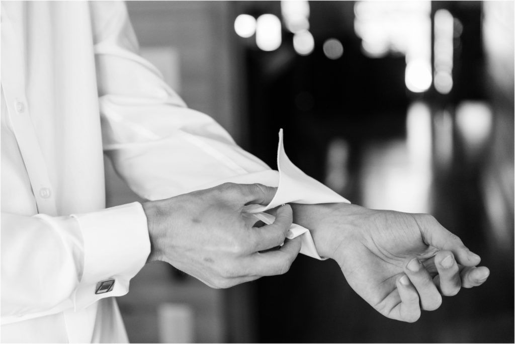 Black and white close-up of hands adjusting shirt cuffs during wedding preparation.