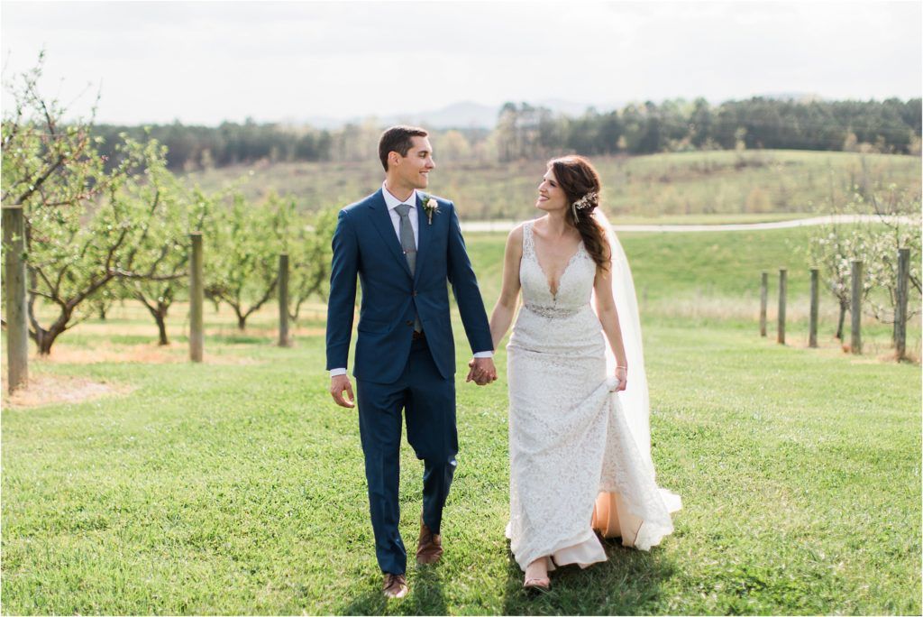 Couple walking hand in hand through vineyard in elegant wedding attire.