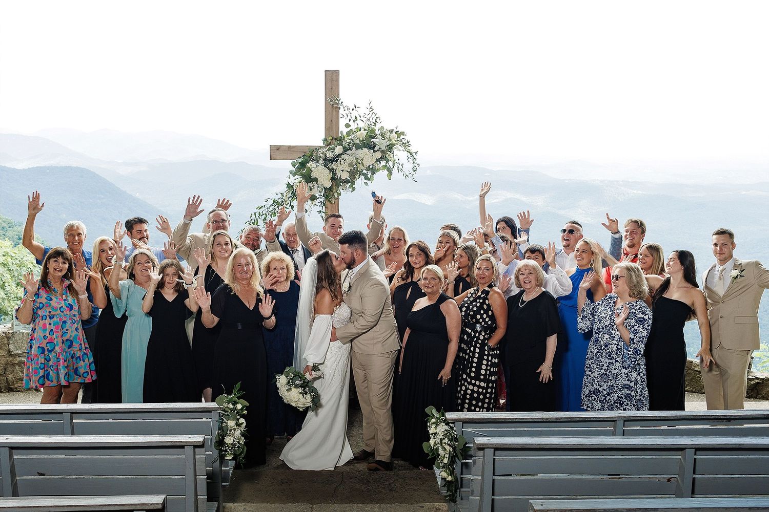 Wedding party and guests celebrating with arms raised at mountain overlook venue.