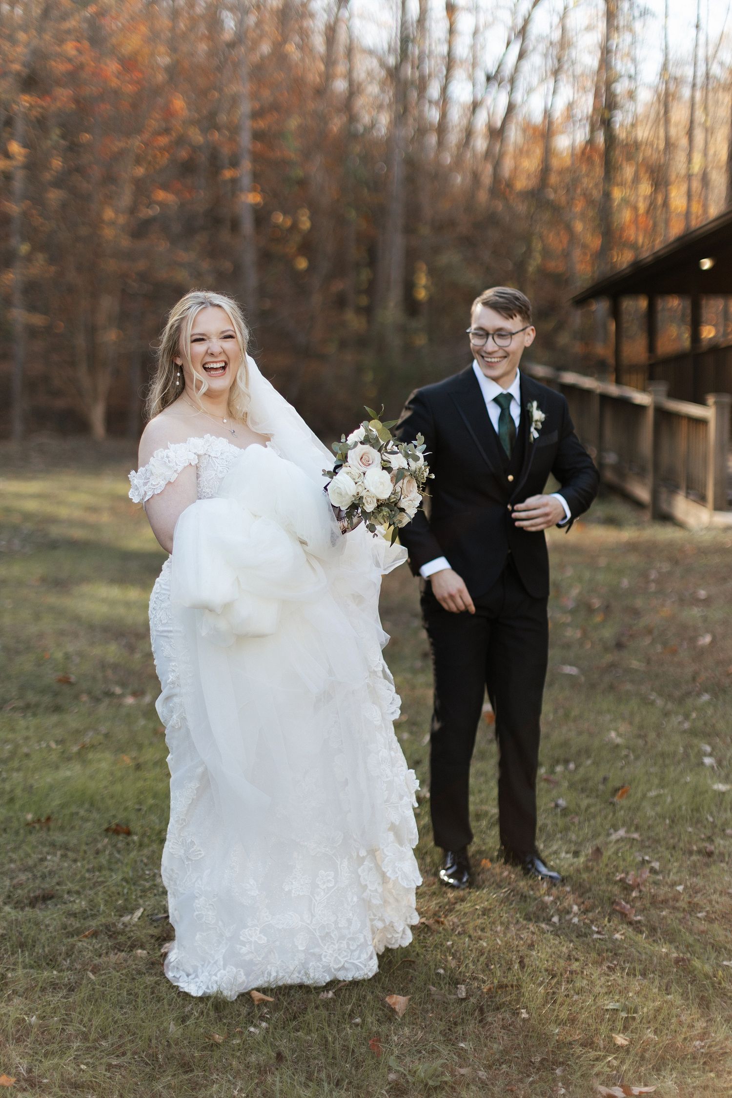 A bride and groom share a joyful moment outdoors during their fall wedding with autumn trees in the background.