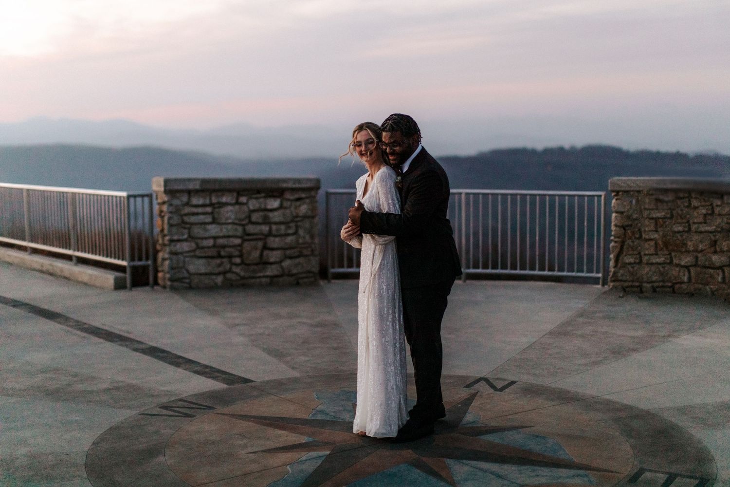 A couple shares an intimate dance at dusk on a mountain viewpoint.