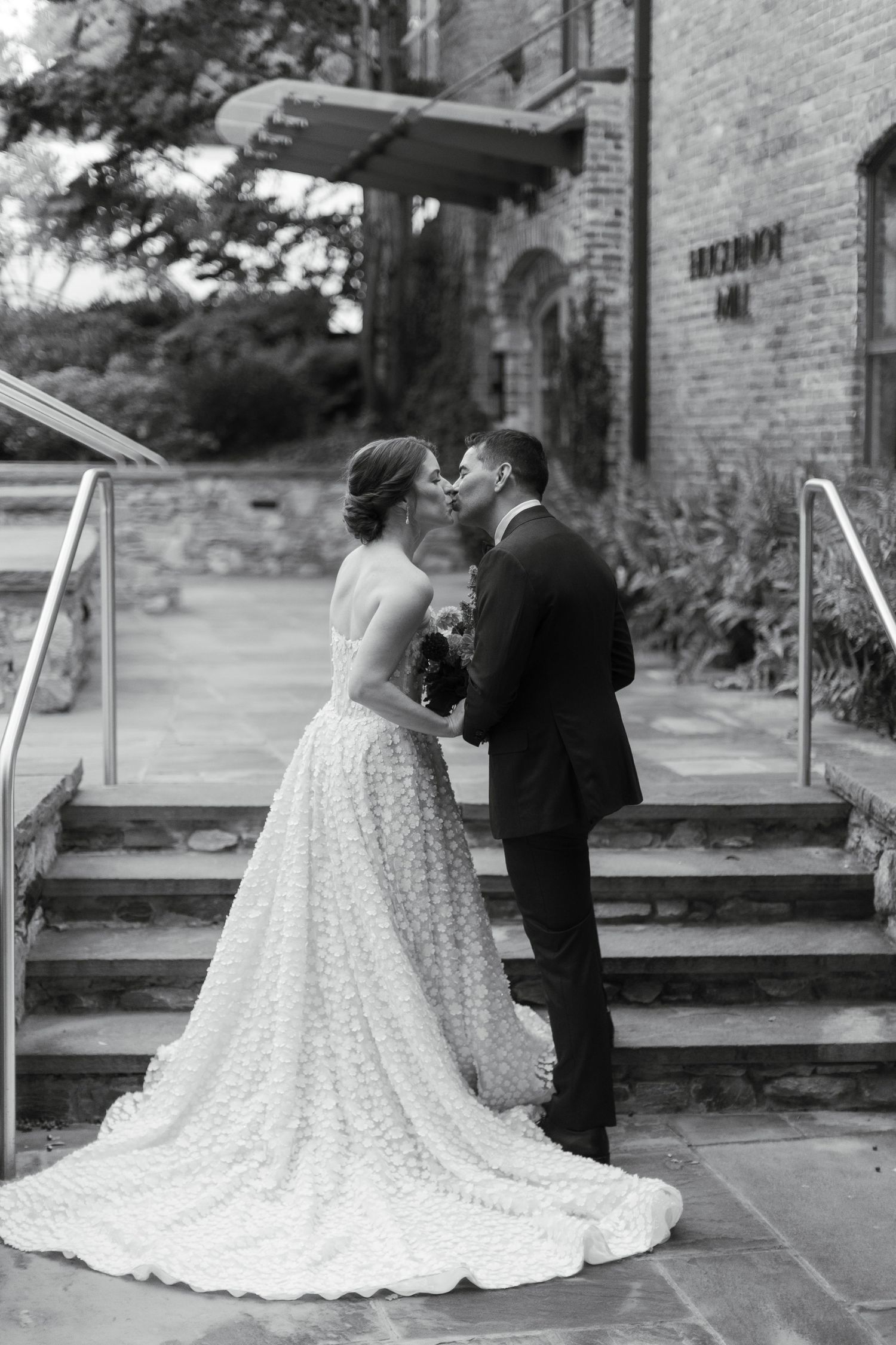 Black and white photo of bride and groom sharing a kiss on stone steps outside the Huguenot Mill and Loft in Greenville, SC.