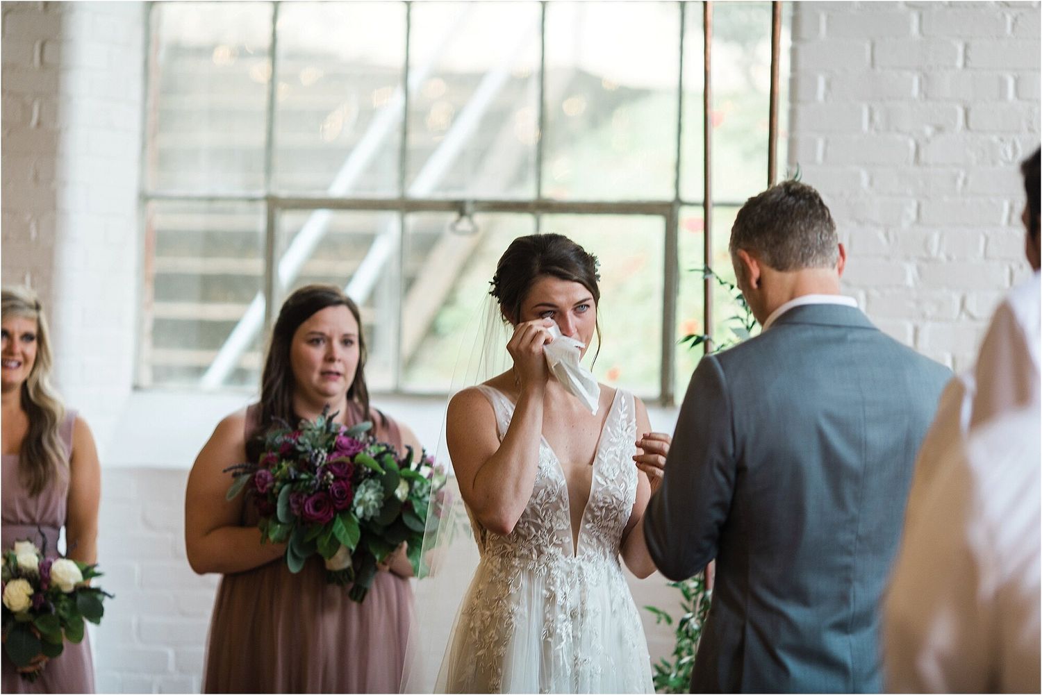 An emotional moment during a wedding ceremony as attendants look on holding purple bouquets.