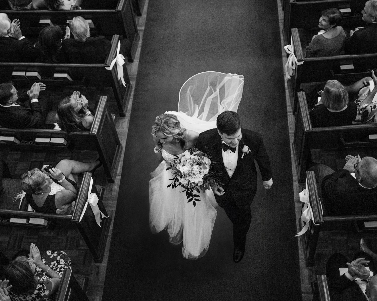 Aerial black and white photo of bride and groom walking down church aisle after wedding ceremony.