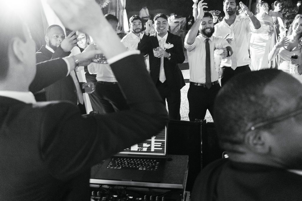 A black and white photo showing guests dancing near a DJ booth at a wedding reception.