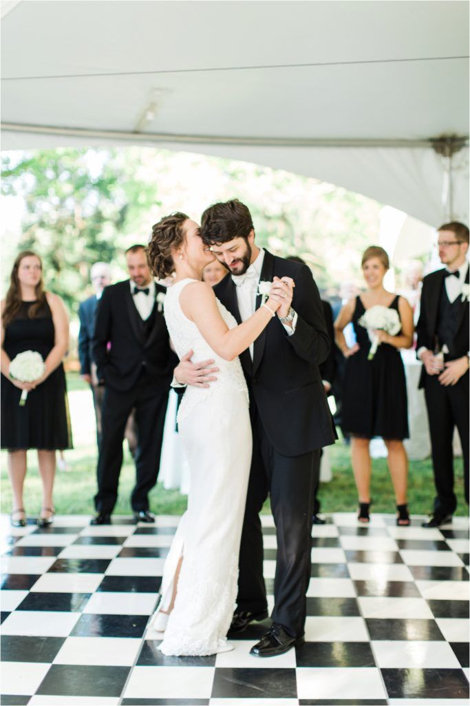 A couple shares their first dance on a black and white checkered dance floor under a tent.