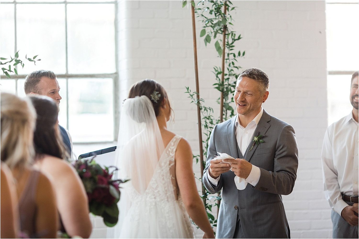 A wedding ceremony in progress in front of large windows with delicate greenery decorations.