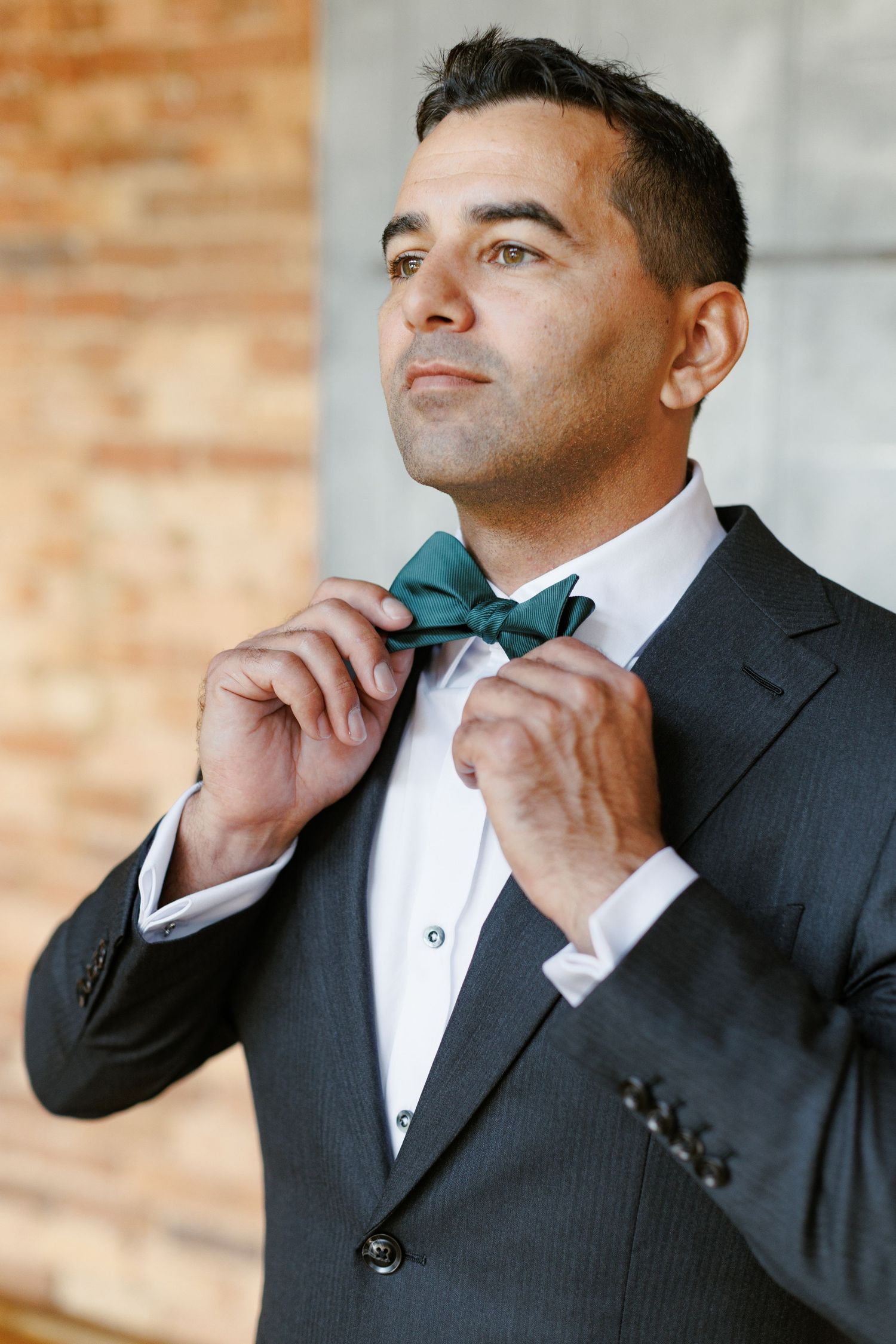 Man in dark suit adjusting green bow tie, elegant formal attire for wedding or special occasion.