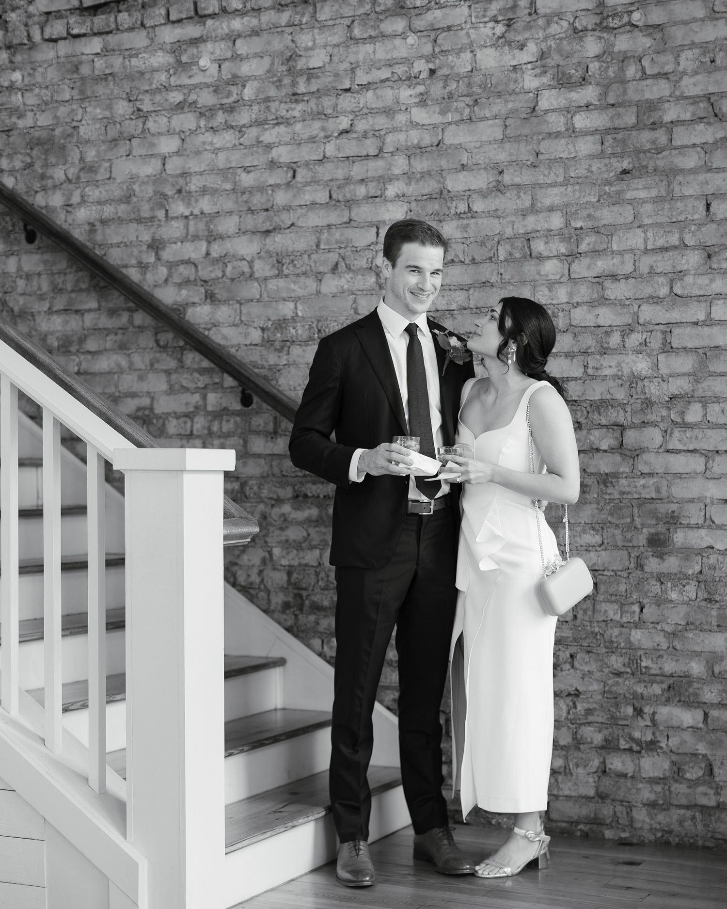A series of black and white photos showing a couple in formal attire looking at their phones against a brick wall.