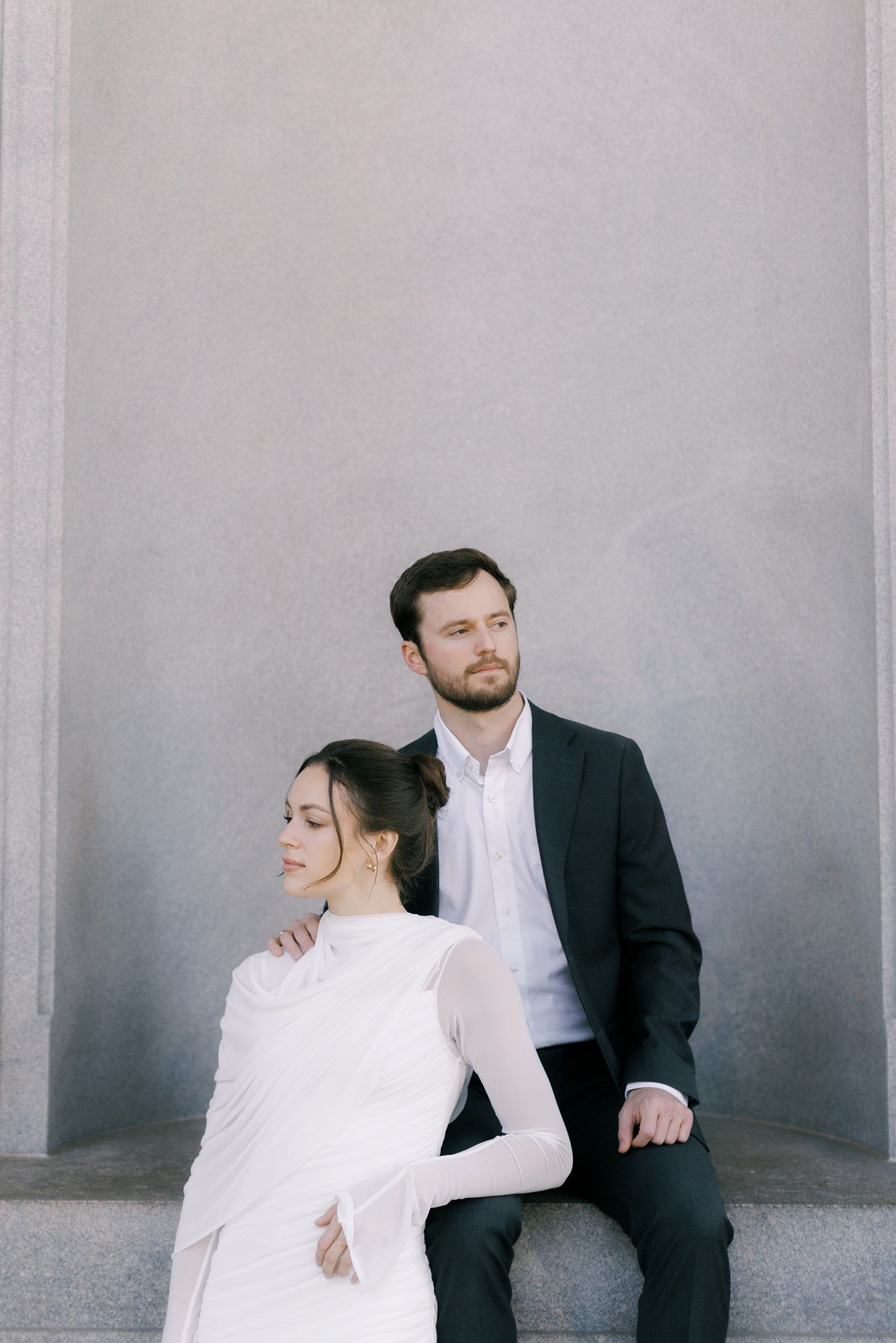 A minimalist photo sequence shows a couple in formal attire sitting and interacting against a gray wall.
