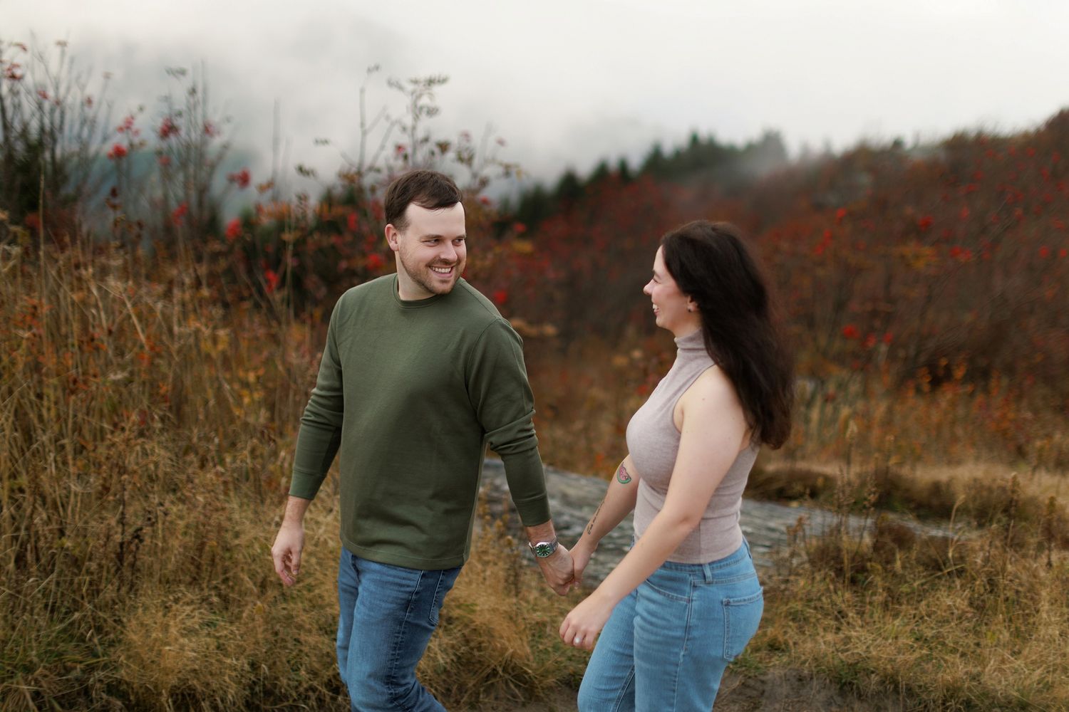 Couple walking through a misty autumn field with mountains in the background.