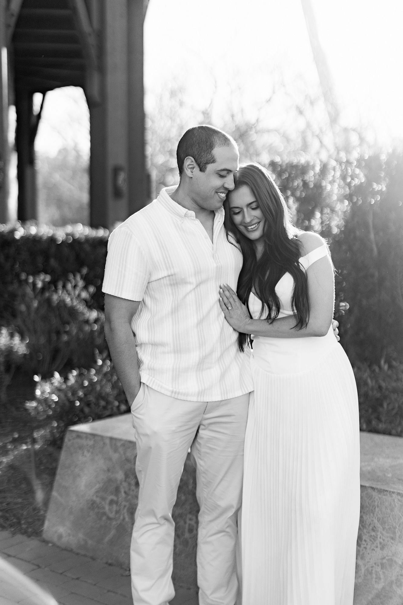 A romantic black and white portrait of a couple in white outfits sharing an intimate moment outdoors.