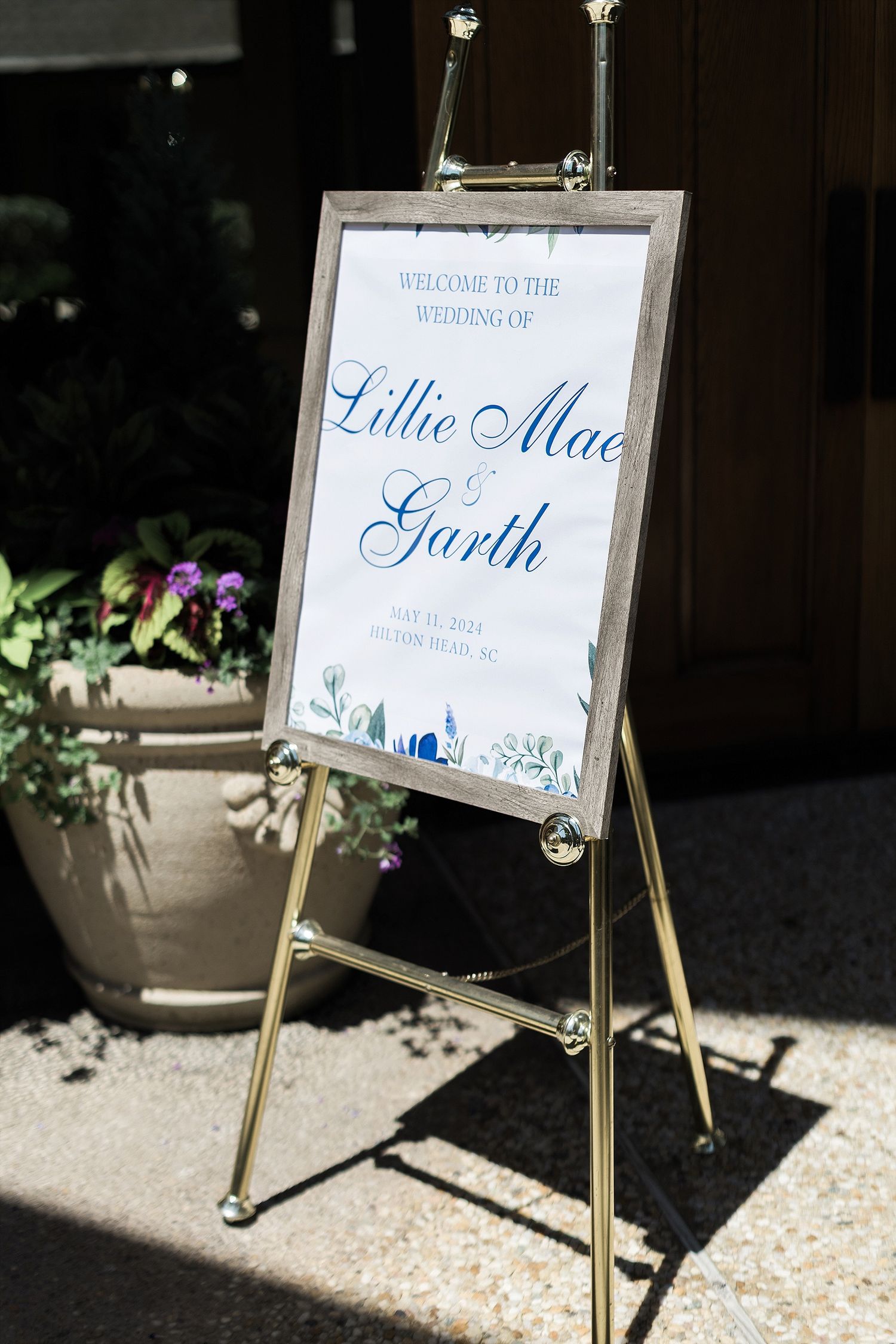 Wedding welcome sign on gold easel with blue calligraphy and floral design.