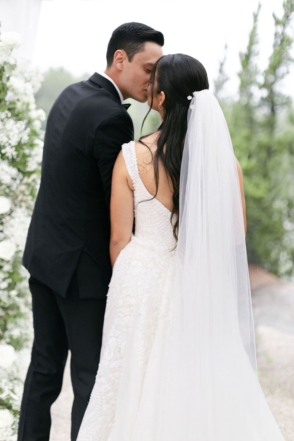 Intimate wedding moment captured among white floral arrangements and greenery.