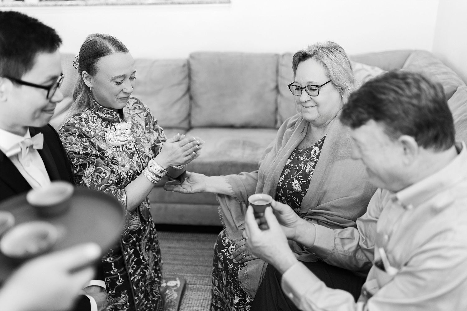 A black and white photograph of people gathered on a sofa playing cards in a casual social setting.