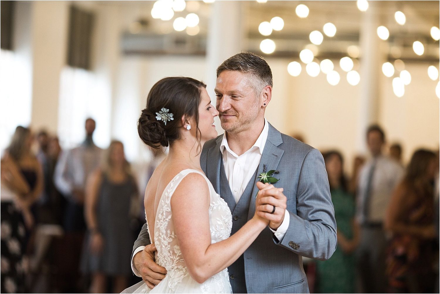A couple shares an intimate moment during their first dance in a warmly lit reception hall.