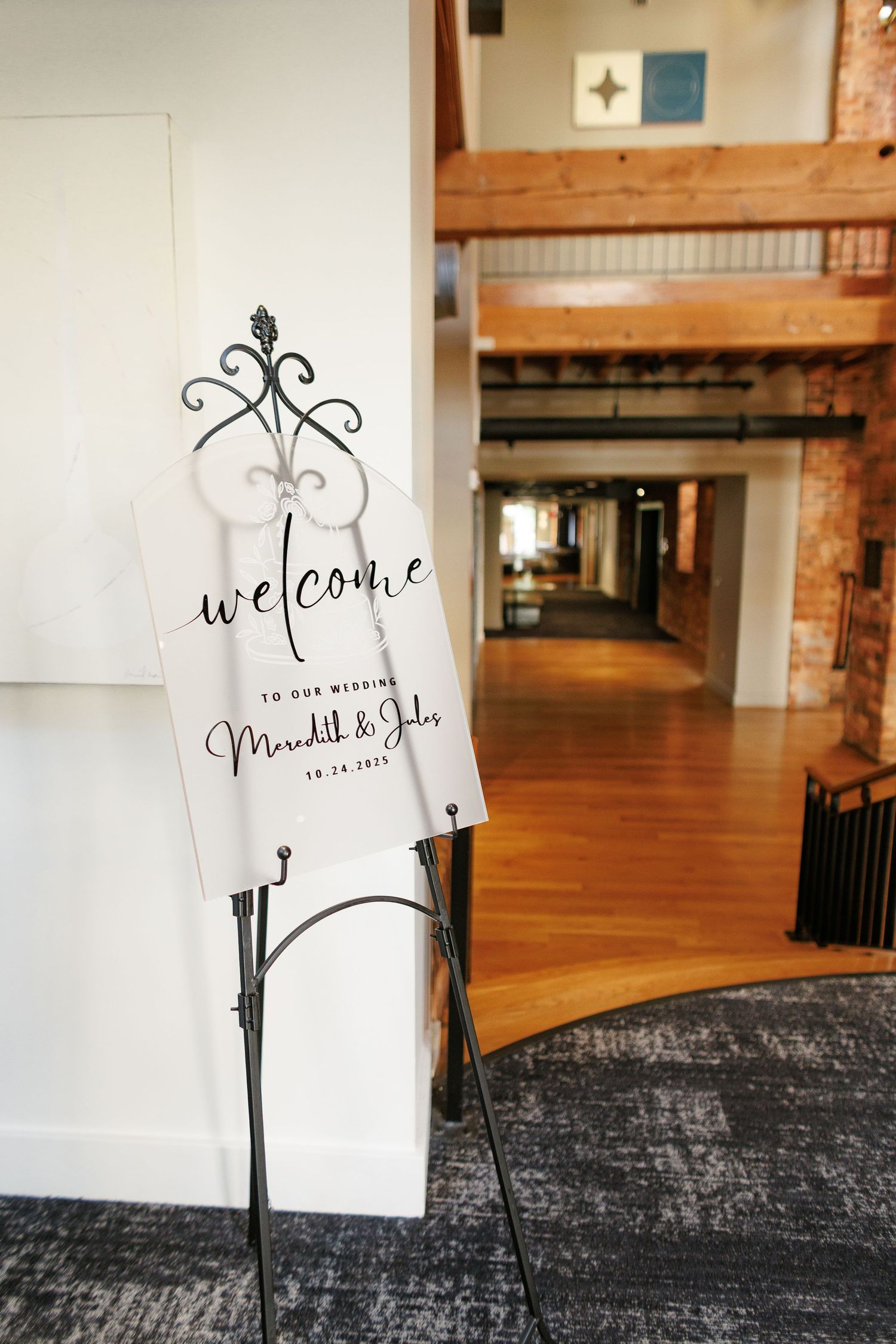Elegant wedding welcome sign for Meredith and Jules on a decorative iron stand in a rustic venue hallway.