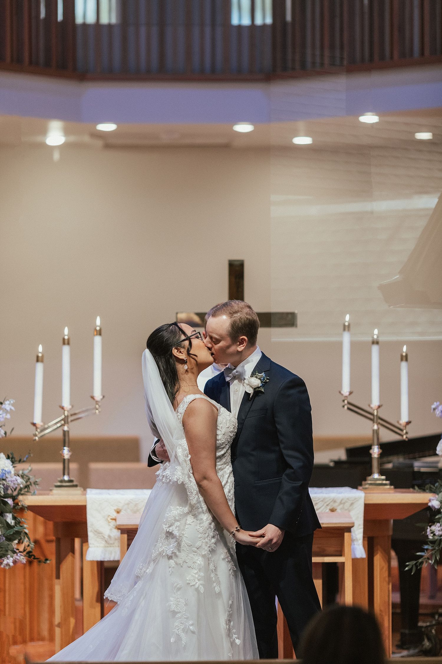 Newlyweds share their first kiss at altar surrounded by candlesticks in church ceremony.