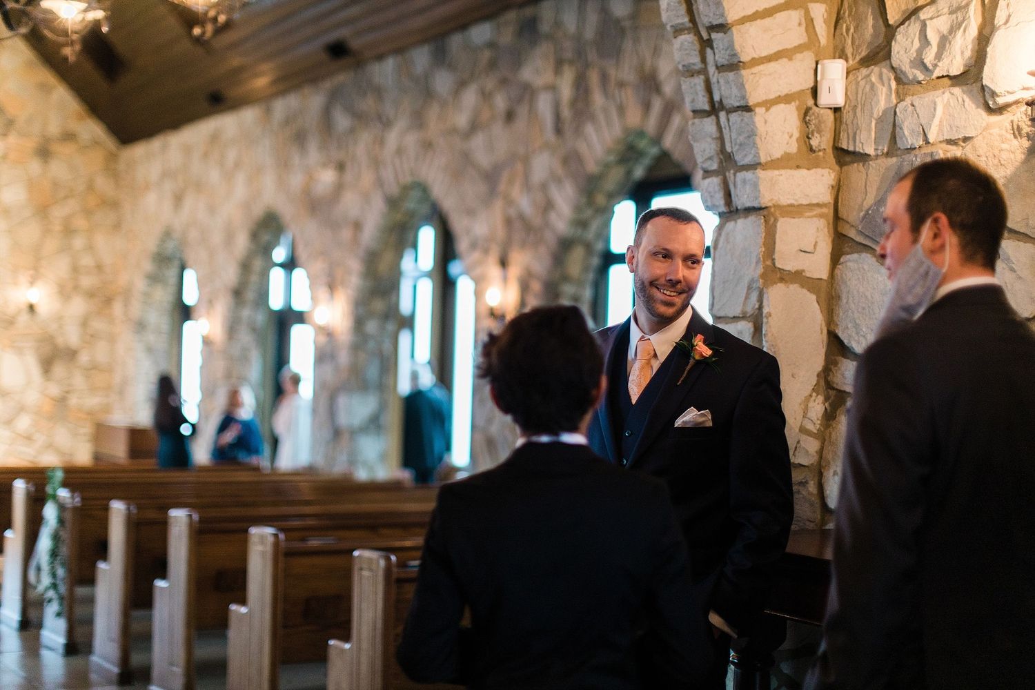 Interior of a stone chapel with stained glass windows during a wedding ceremony.