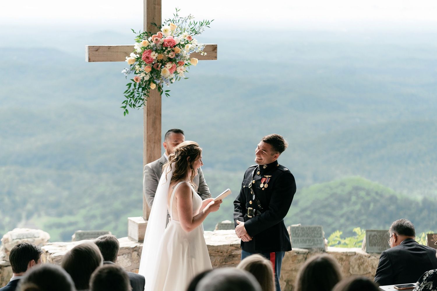 Scenic mountaintop wedding ceremony with a wooden cross decorated with flowers overlooking mountain vistas and valleys.