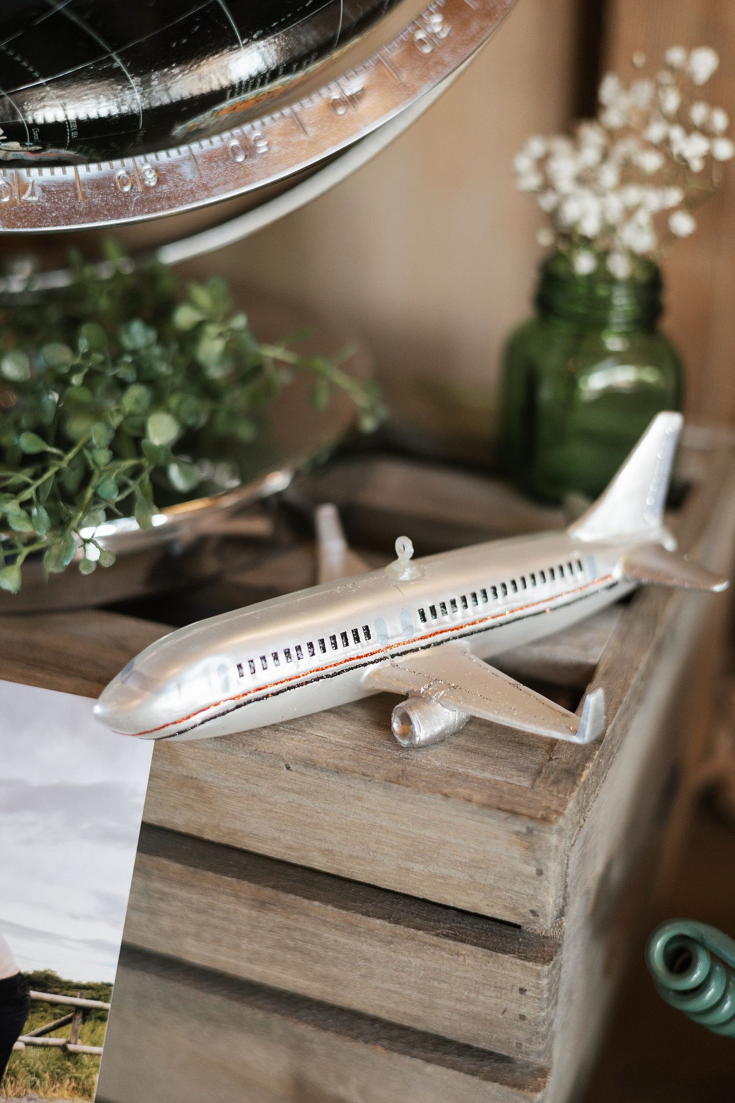 Small decorative toy airplane model sits on wooden crates with green plants and glassware in background.