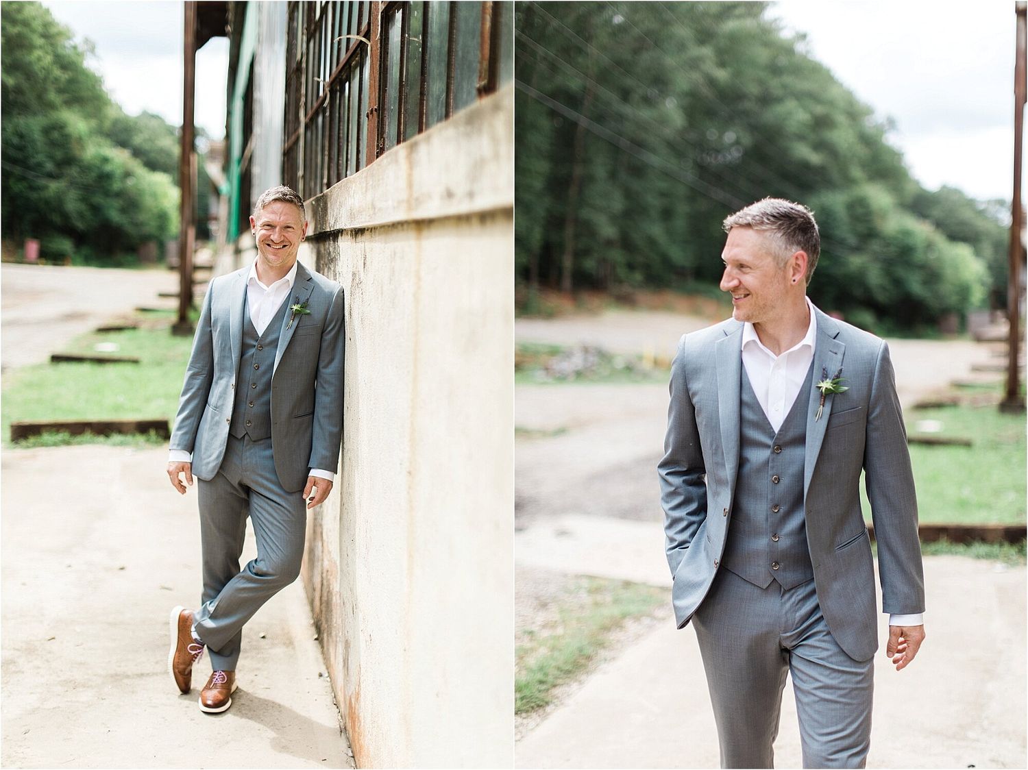 A groom in a grey three-piece suit poses casually against an industrial building wall.