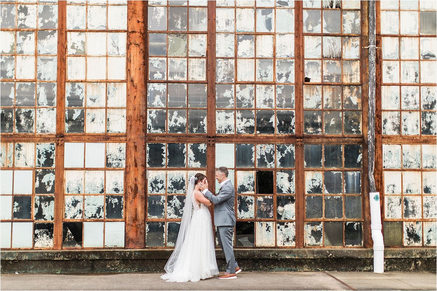 Romantic wedding photo against vintage industrial windows with weathered frames.